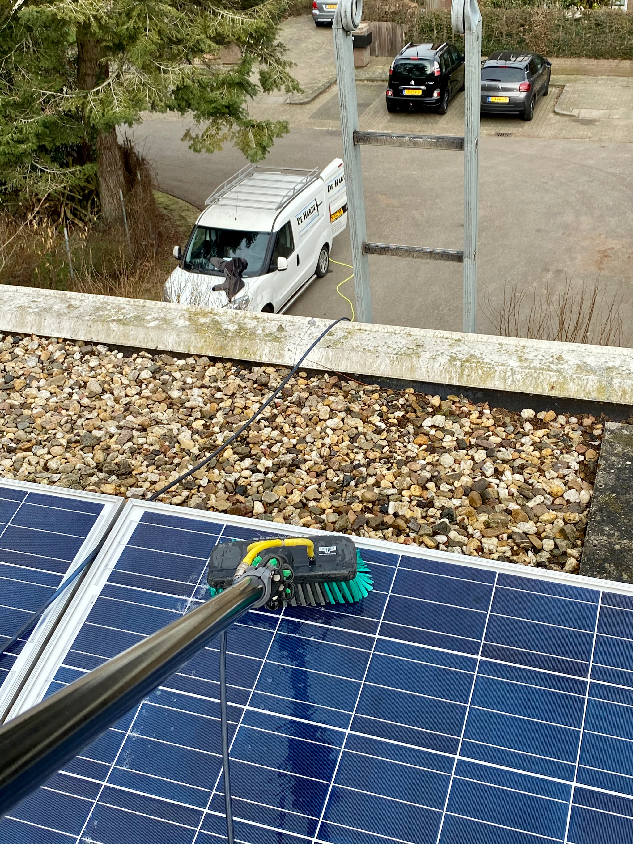 Zonnepanelen reinigen met een borstel op een plat dak, de bus beneden geparkeerd