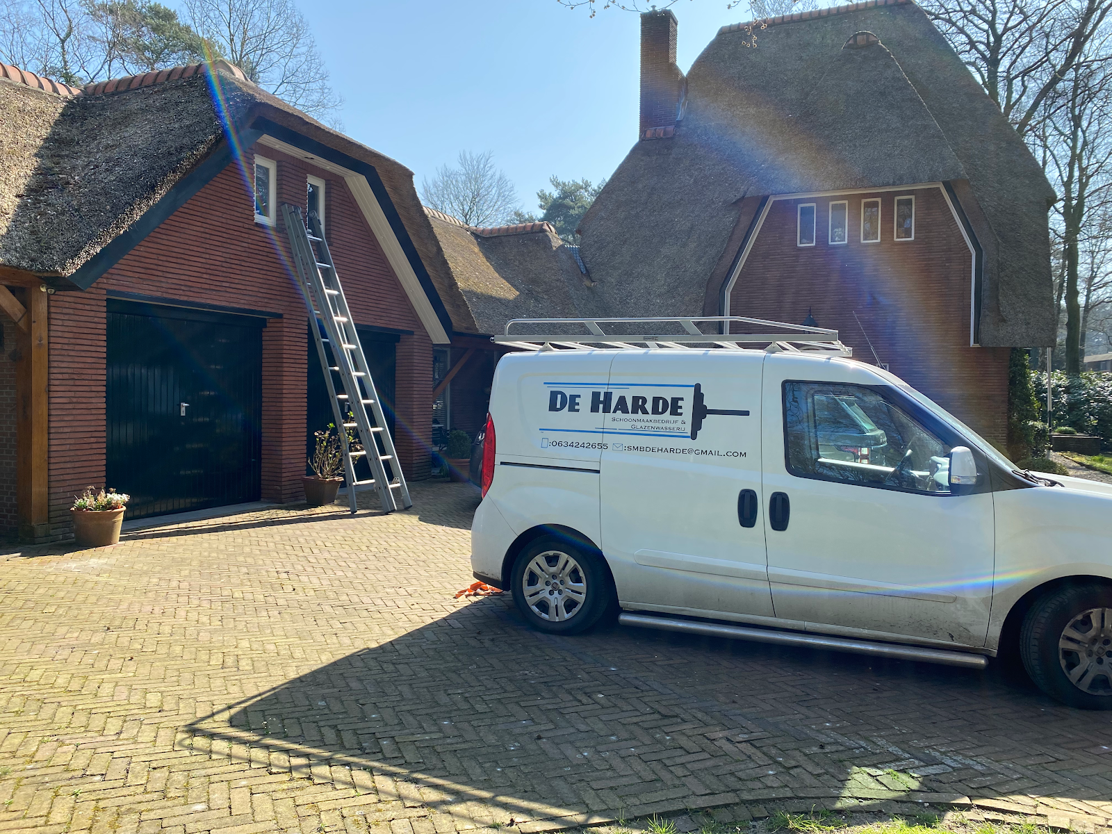 De witte bus van De Harde met ladder, bij een villa met rieten dak